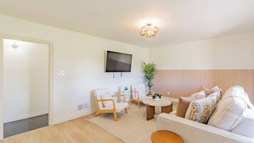 A modern living room with a sofa, chairs, a coffee table, a TV mounted on the wall, and a plant.