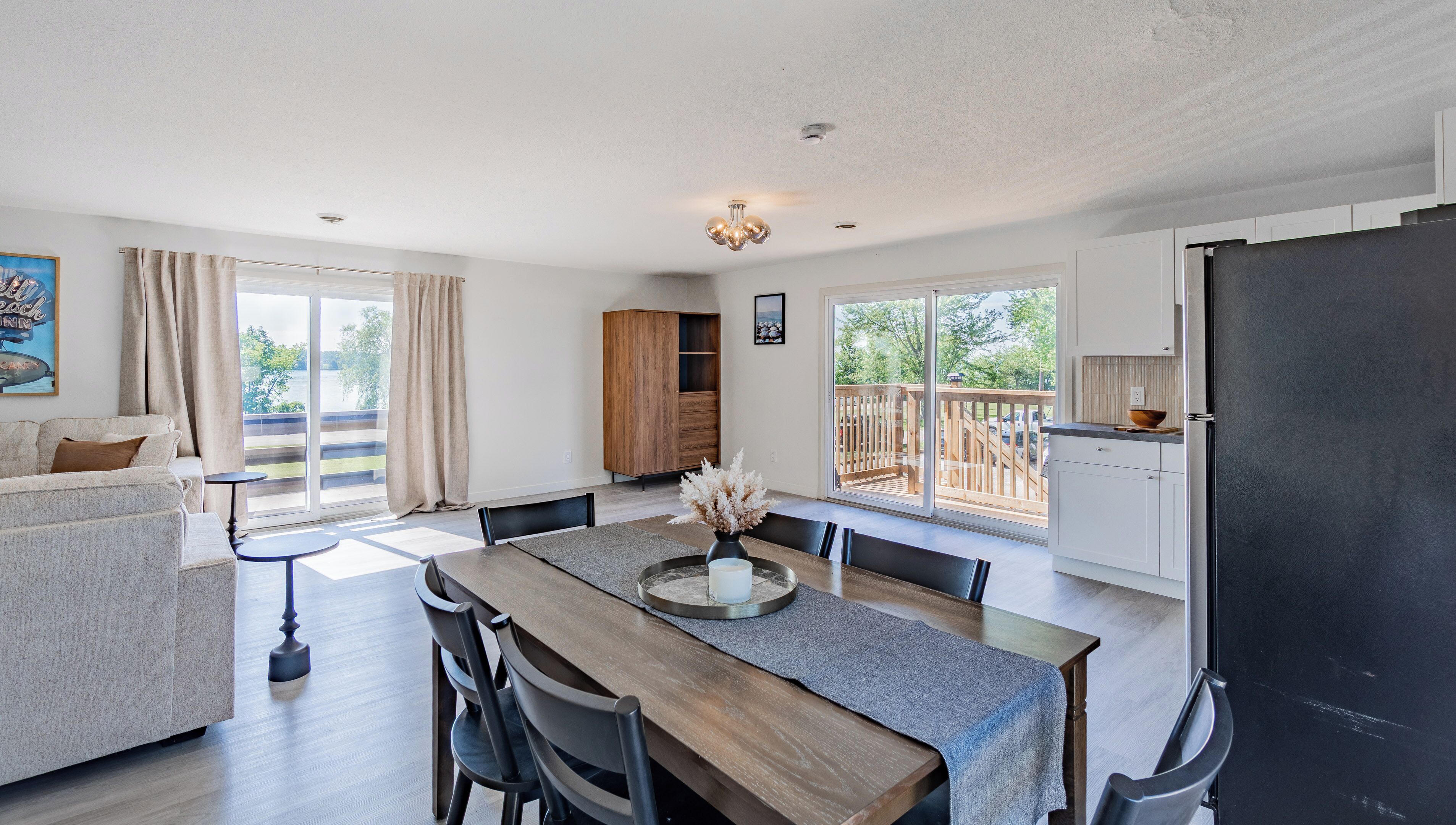 A spacious living area with a dining table, chairs, a sofa, a wooden cabinet, and a sliding glass door leading to a balcony.