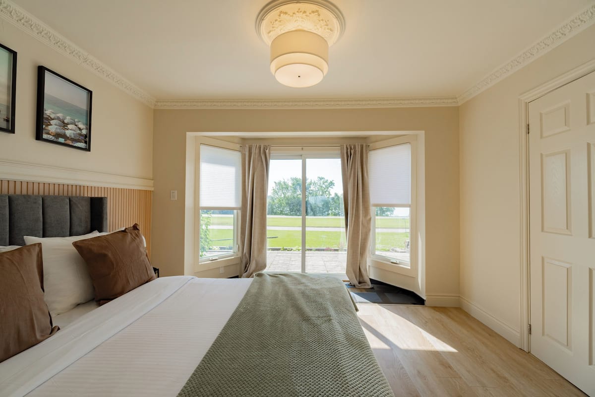 Ein Schlafzimmer mit Bett, einem Vorhangfenster, einer Tür und Blick ins Freie.