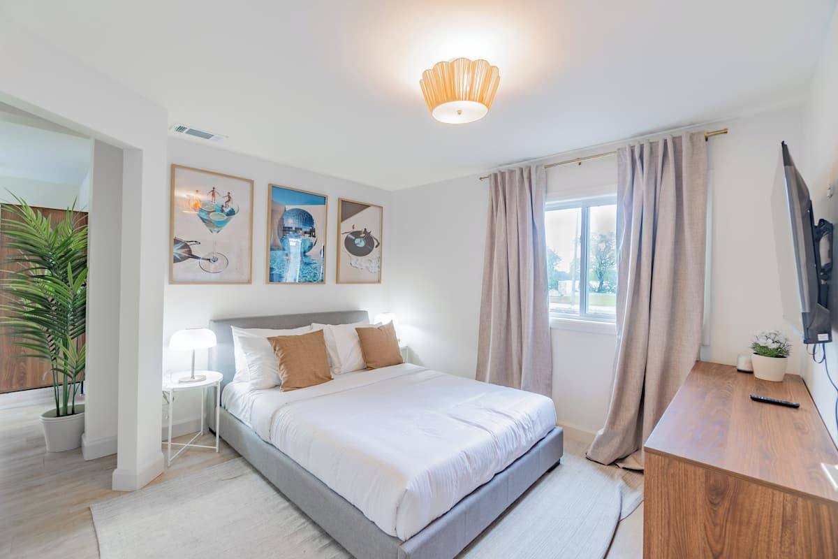 Ein modernes Schlafzimmer mit Bett, Nachttischen, einem Schreibtisch, einem Fernseher und Kunstwerken an der Wand.