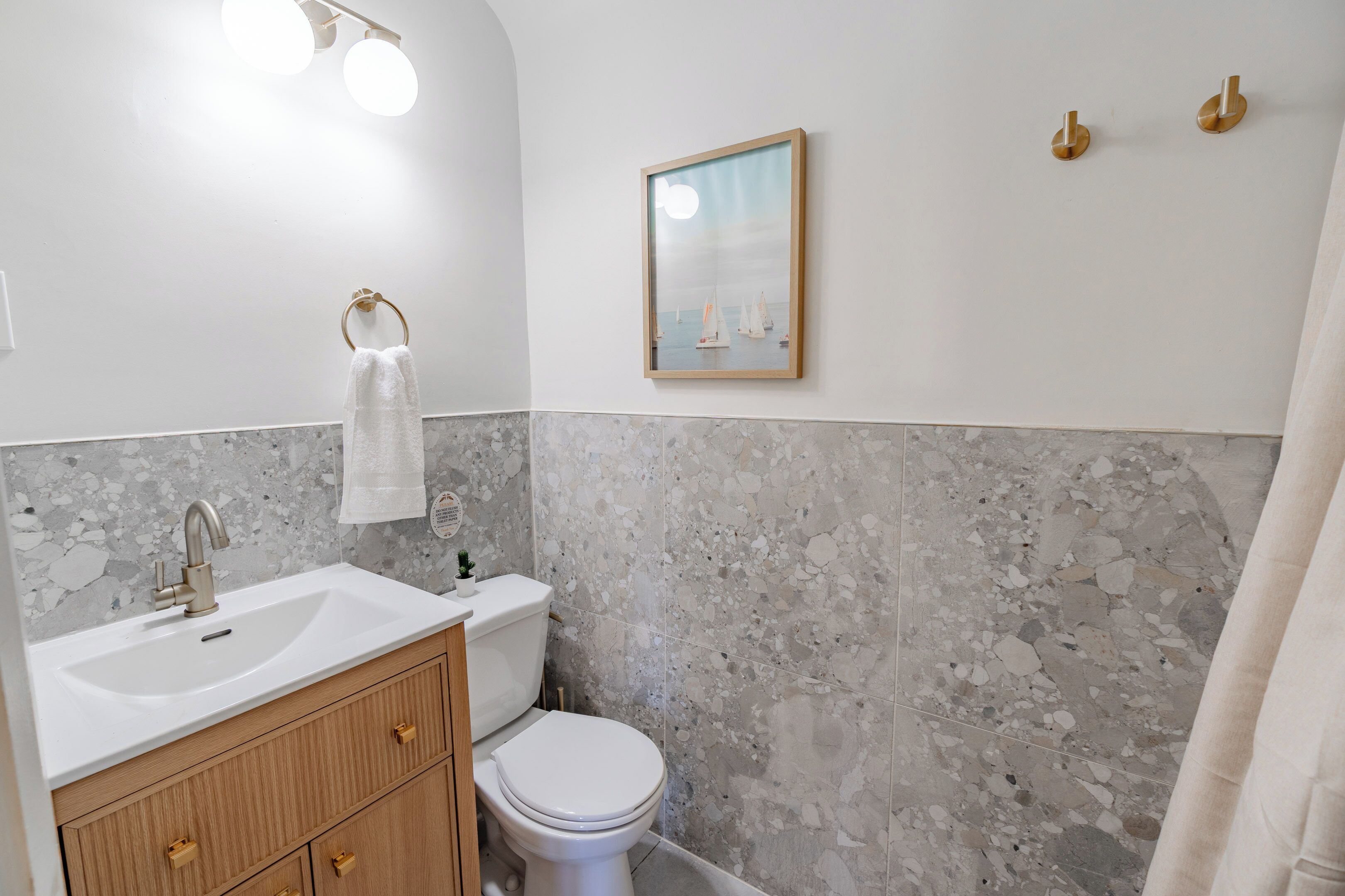 A bathroom with a marble backsplash, a white sink, a toilet, and a framed picture on the wall.