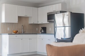 Eine moderne Küche mit weißen Schränken, einem Edelstahlkühlschrank und einer Kaffeemaschine.