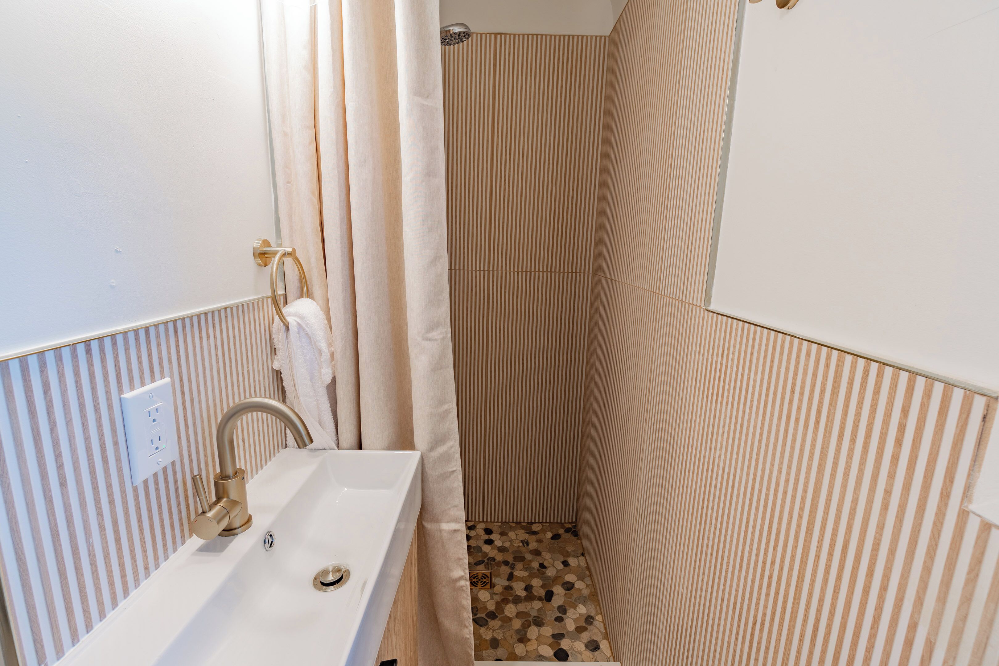 Un baño con un lavabo blanco, ducha con paredes a rayas y suelo estampado.