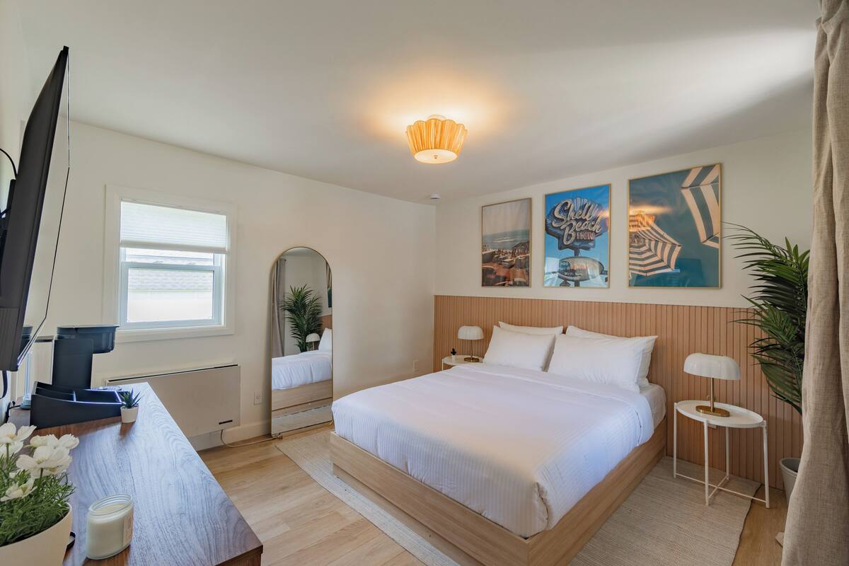 Ein Schlafzimmer mit einem großen Bett, einem Schreibtisch mit Computer, einem Spiegel und Kunstwerken an der Wand.