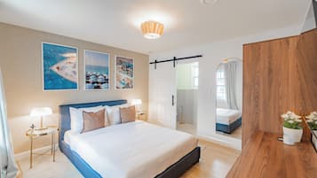 Une chambre d’hôtel moderne avec un grand lit, des tables de chevet avec des lampes, une commode en bois et des œuvres d’art accrochées aux murs.