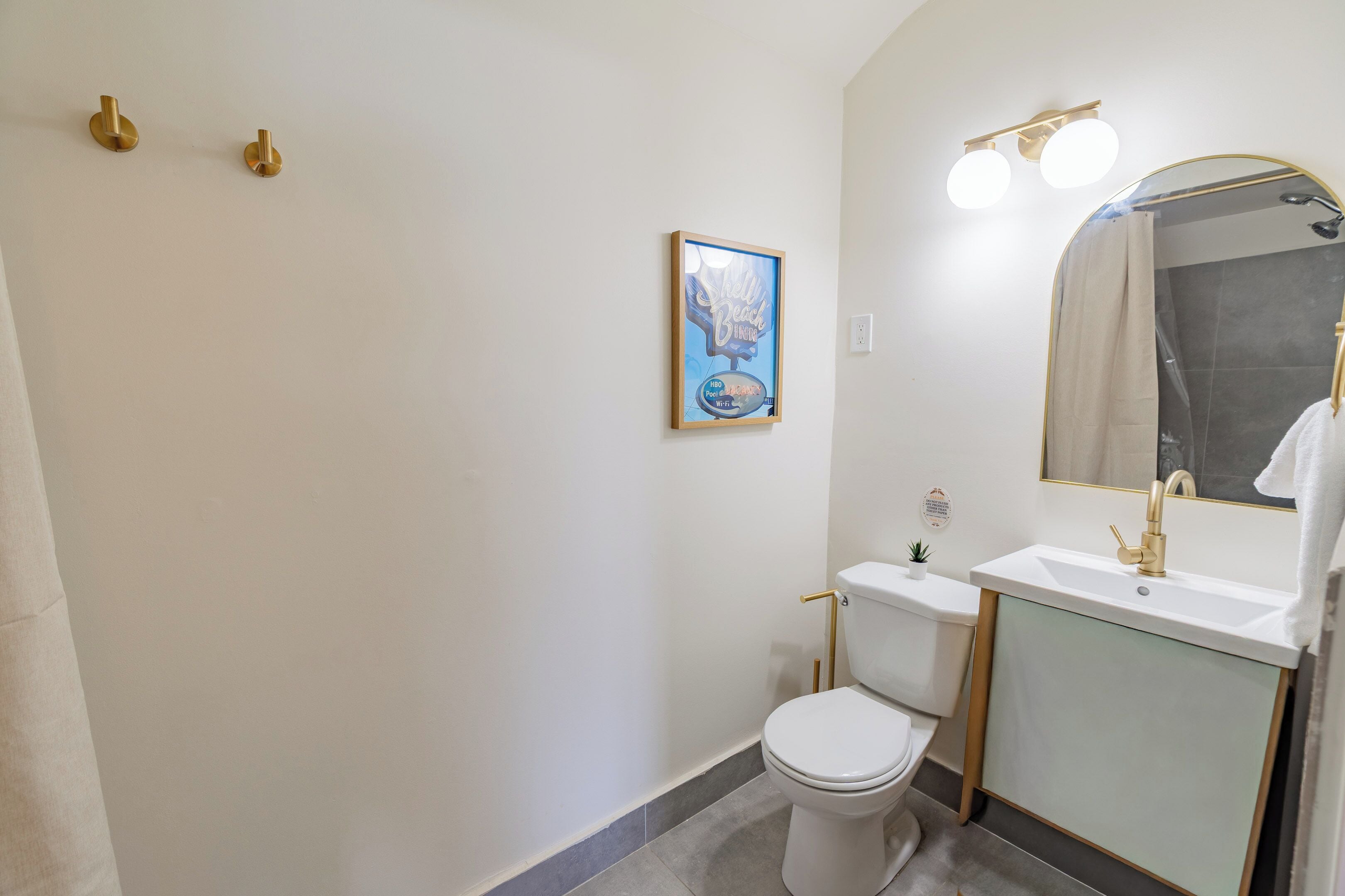A bathroom with a toilet, sink, mirror, and a framed picture on the wall.