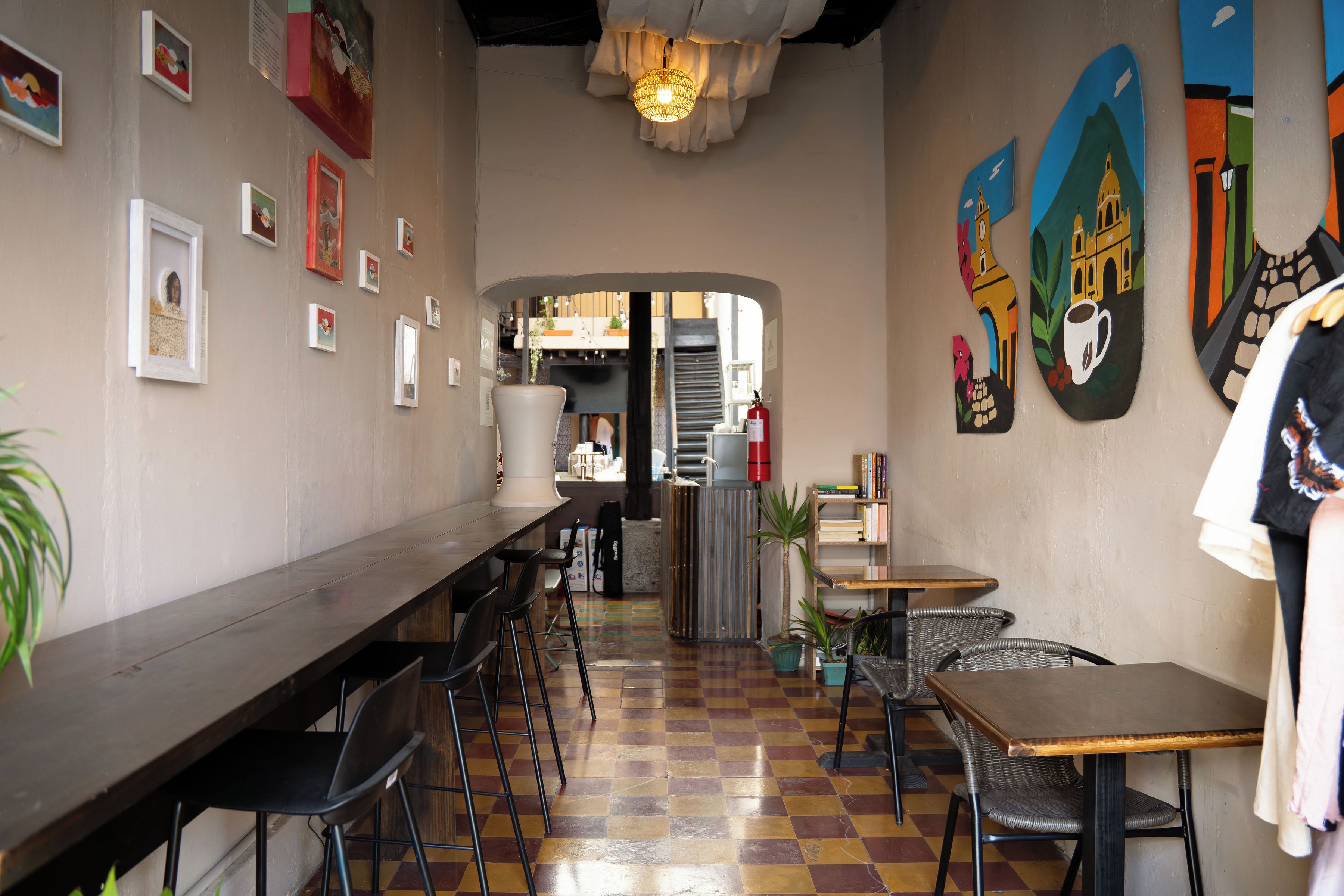 A café interior with a long counter, multiple chairs, a fire extinguisher, and artwork on the walls.
