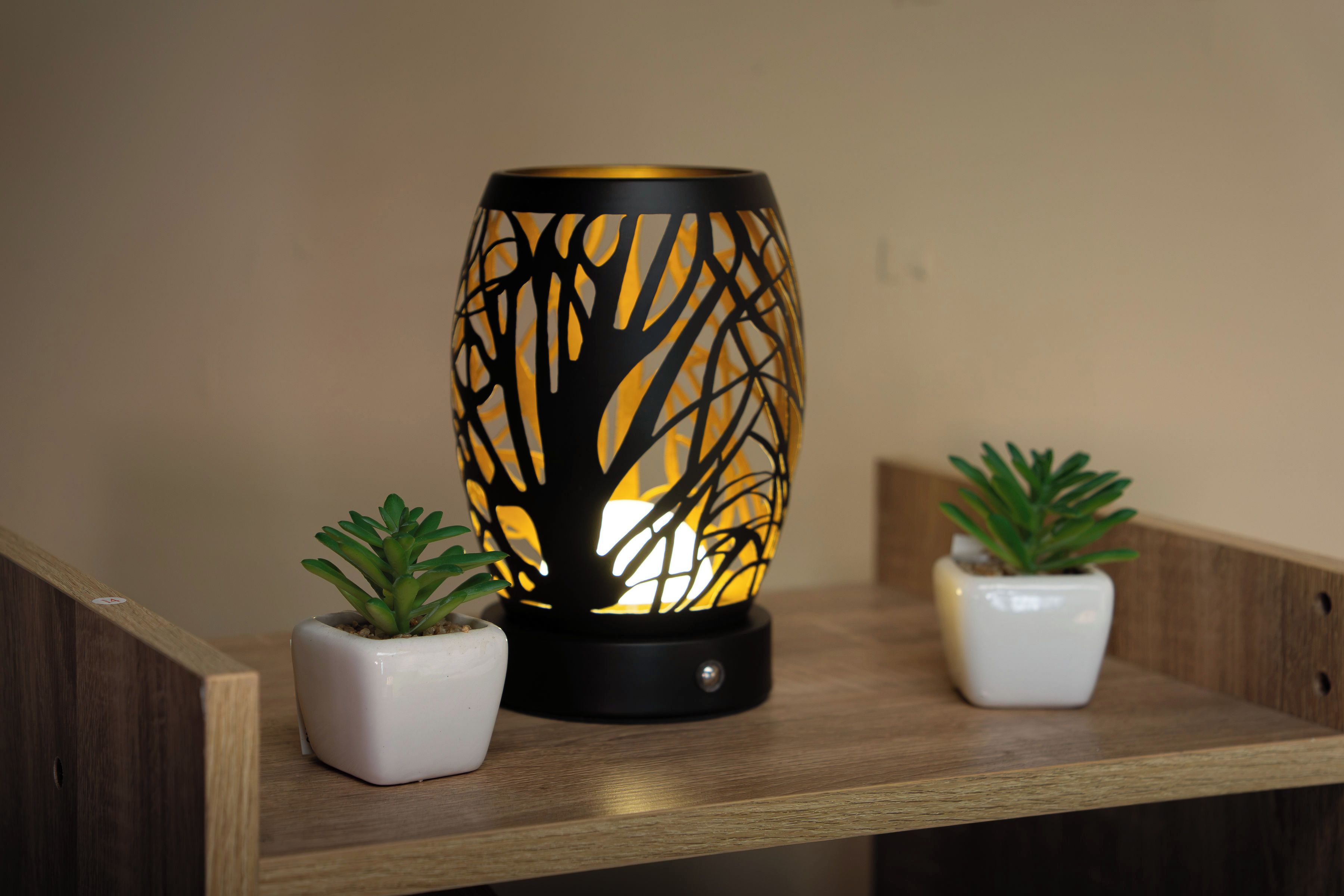 Une étagère en bois surmontée d’une lampe décorative arborant un motif d’arbre, et flanquée de deux plantes en pot.