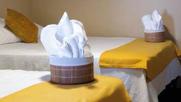 Duas camas com roupa de cama branca e um cobertor amarelo, cada uma com uma caixa de lenços na mesinha de cabeceira.