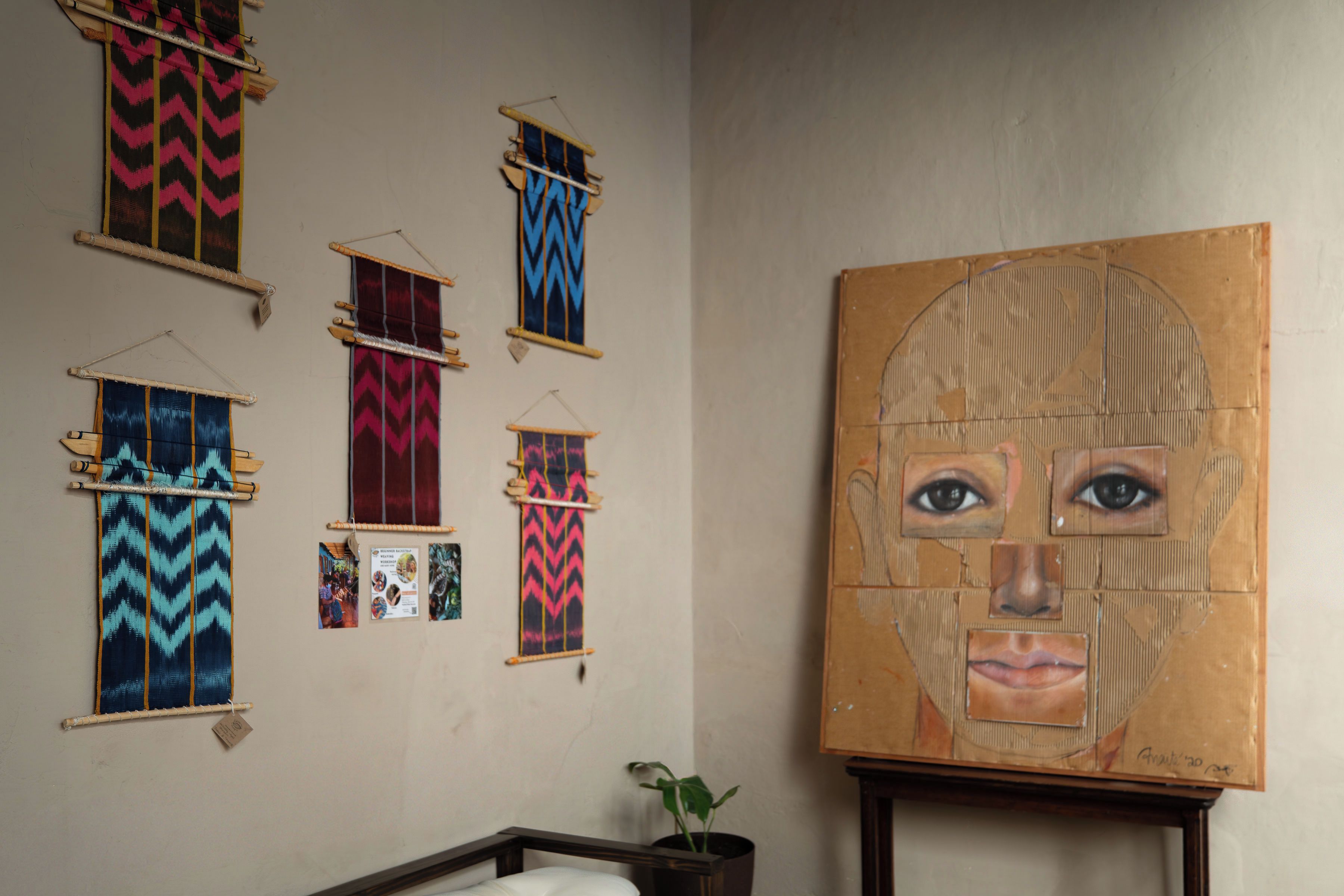 Una habitación con un cuadro grande, varios textiles estampados en la pared y una cama con una planta a su lado.