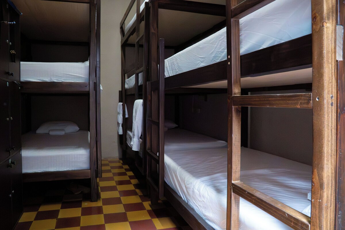 A dormitory room with bunk beds, a checkered floor, and a wardrobe.