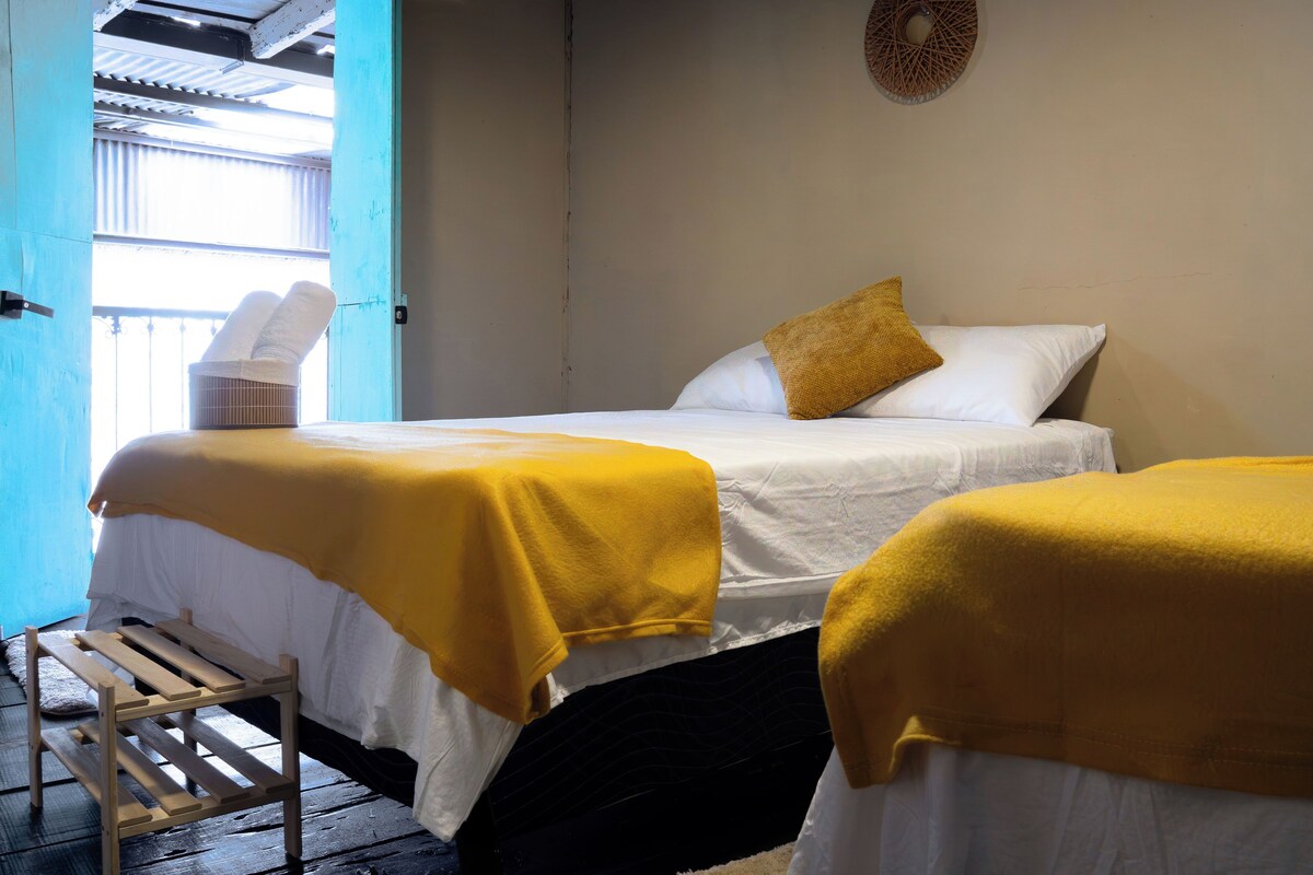 A room with two beds, each with a yellow blanket, a bedside table, and a small heater.
