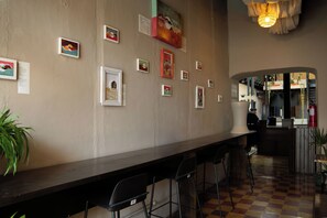 Una zona de bar con una barra larga, varios taburetes y cuadros en la pared.