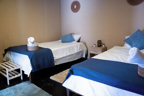 Habitación de hotel con dos camas individuales, una mesita pequeña, una silla y una mesita de noche con lámpara.