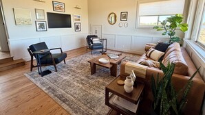 Uma sala de estar com sofá, cadeiras, mesa de centro e televisão.