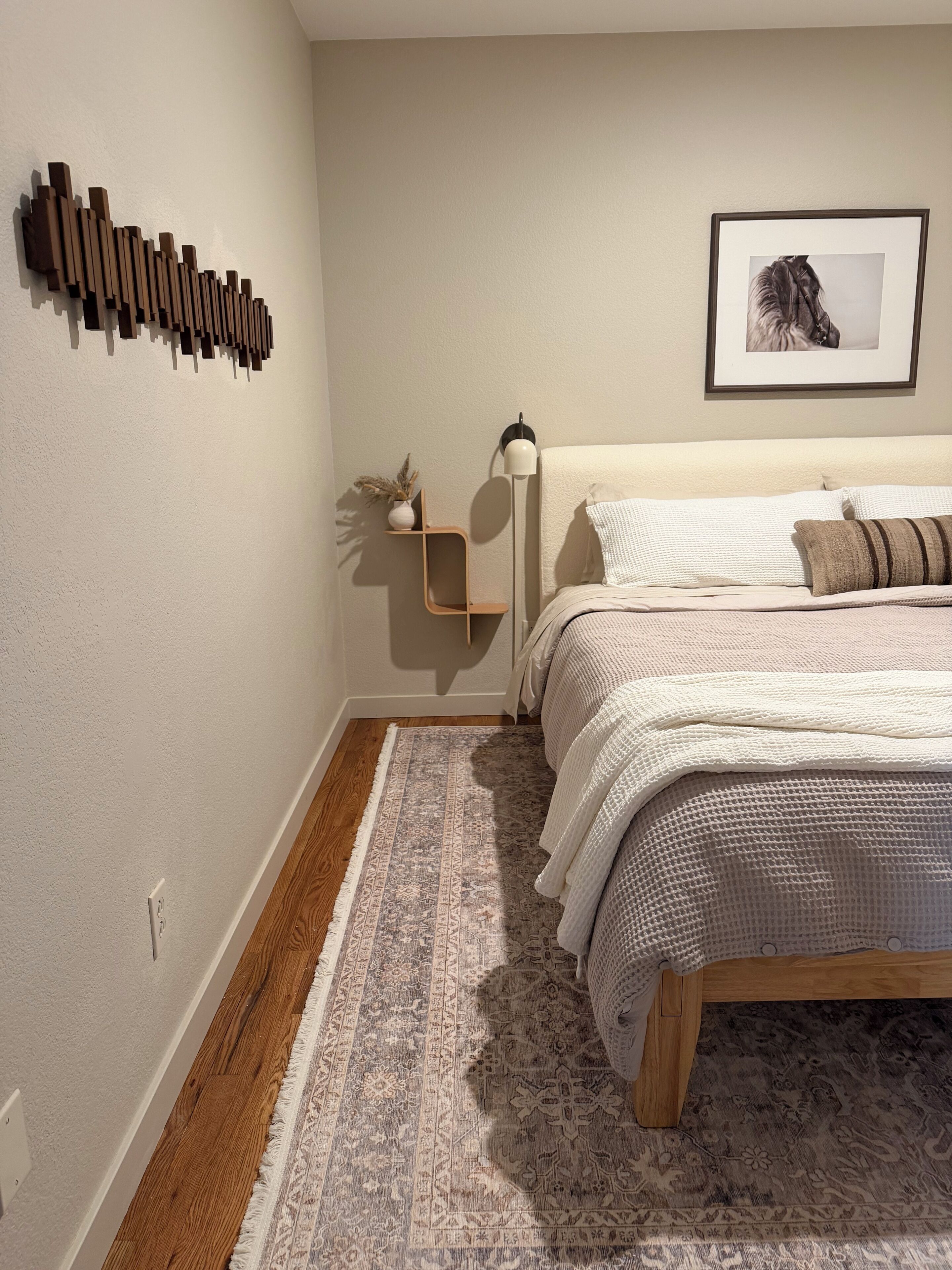Ein Schlafzimmer mit Bett, Nachttisch, Stehlampe, Teppich und einer Wandleuchte.