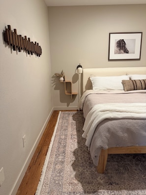 Un dormitorio con cama, mesita de noche, lámpara de pie, alfombra y aplique de pared.