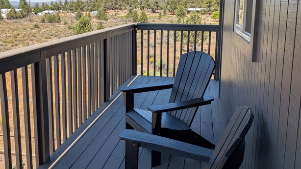 Um deck de madeira com duas cadeiras Adirondack e vista para uma paisagem rural.