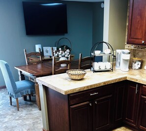 A kitchen with a dining table, chairs, a coffee maker, and a flat-screen TV mounted on the wall.