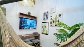 A room with a TV mounted on the wall, a wooden desk, a bench, and several potted plants.