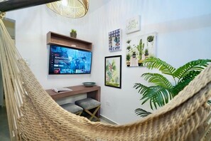 Una habitación con televisión montada en la pared, un escritorio de madera, un banco y varias plantas en macetas.