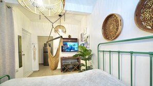 A bedroom with a bed, a hanging chair, a television, and a green railing.