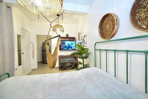 Un dormitorio con cama, una silla colgante, un televisor y un barandal verde.