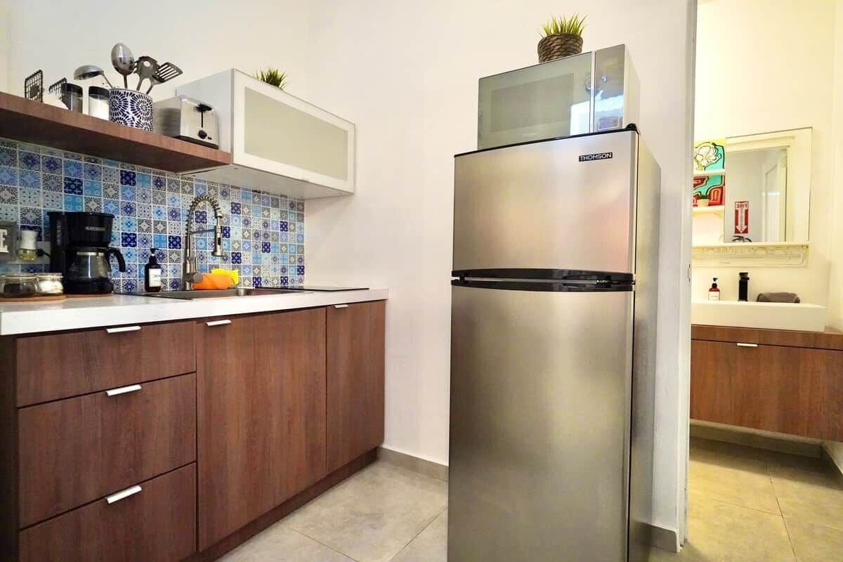 Eine Küche mit einem Edelstahlkühlschrank, Holzschränken, einer gefliesten Spritzschutzwand und einer Mikrowelle auf der Arbeitsfläche.