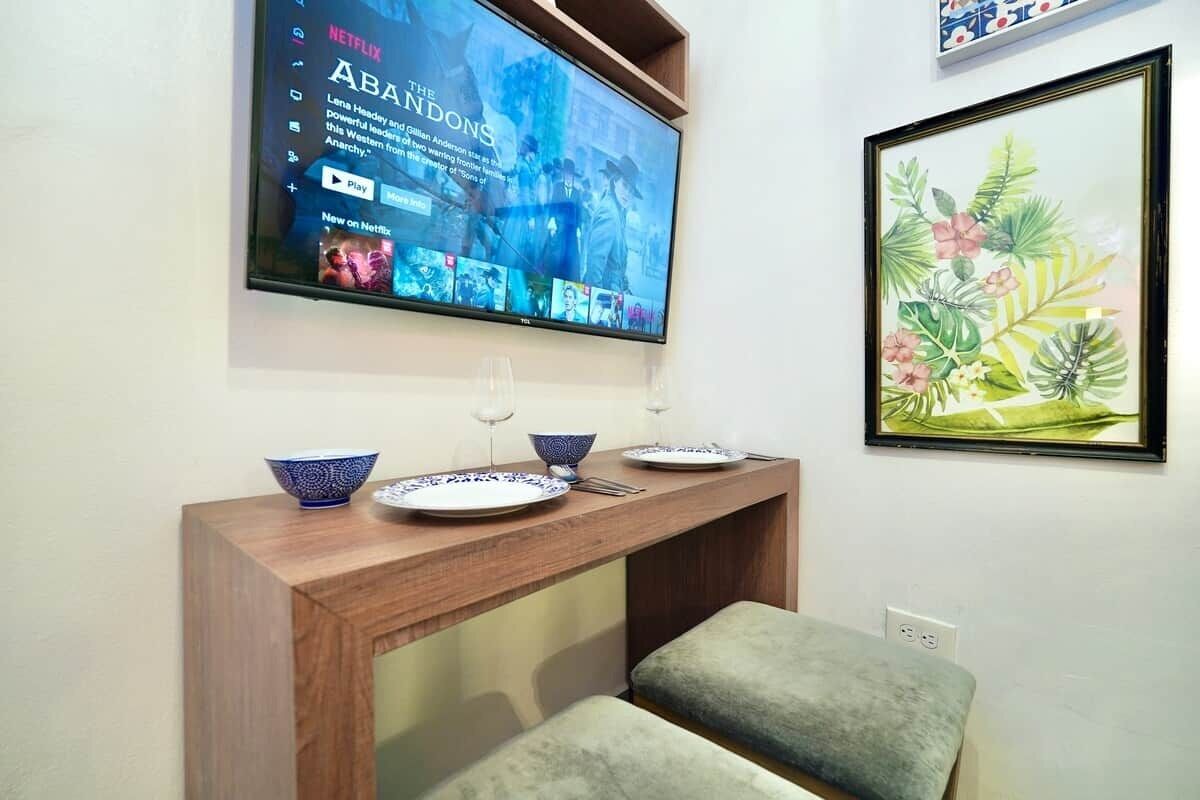 Una habitación con una consola de madera, un televisor montado en la pared y una obra de arte floral enmarcada.