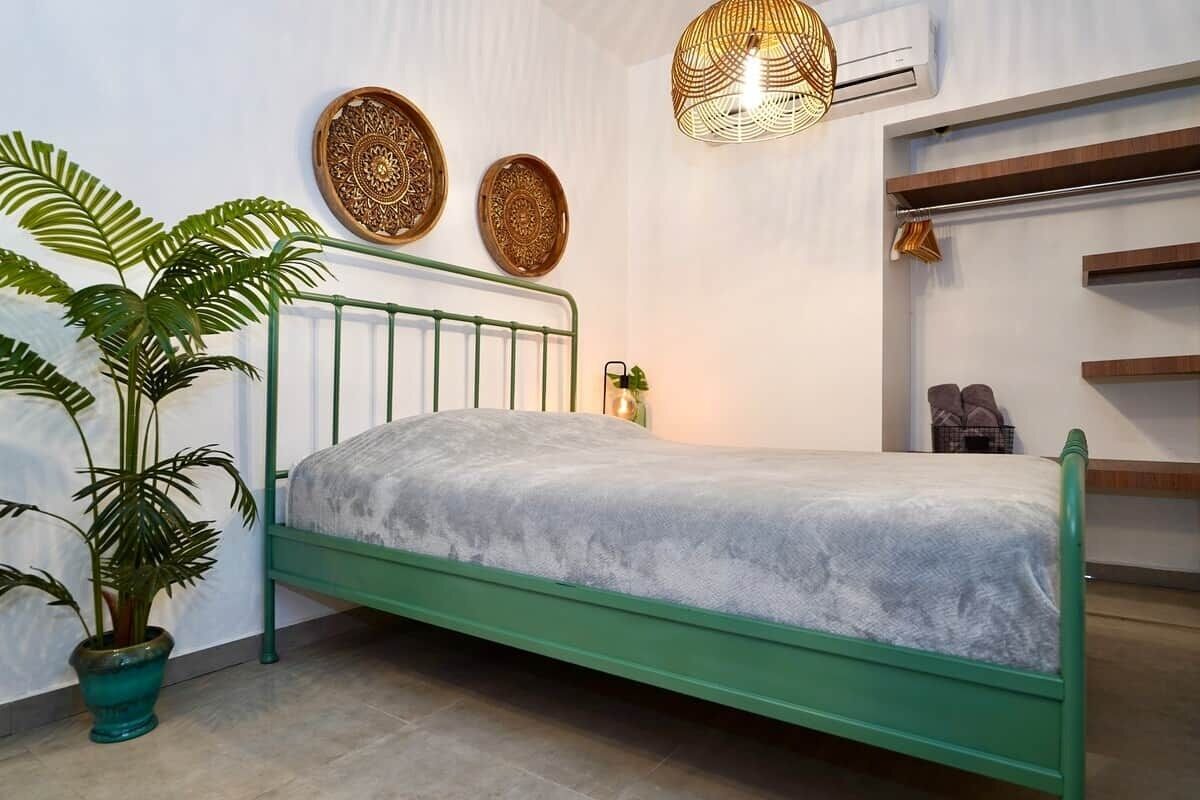 A bed with a green metal frame, a potted plant, decorative wall plates, and a hanging light fixture.