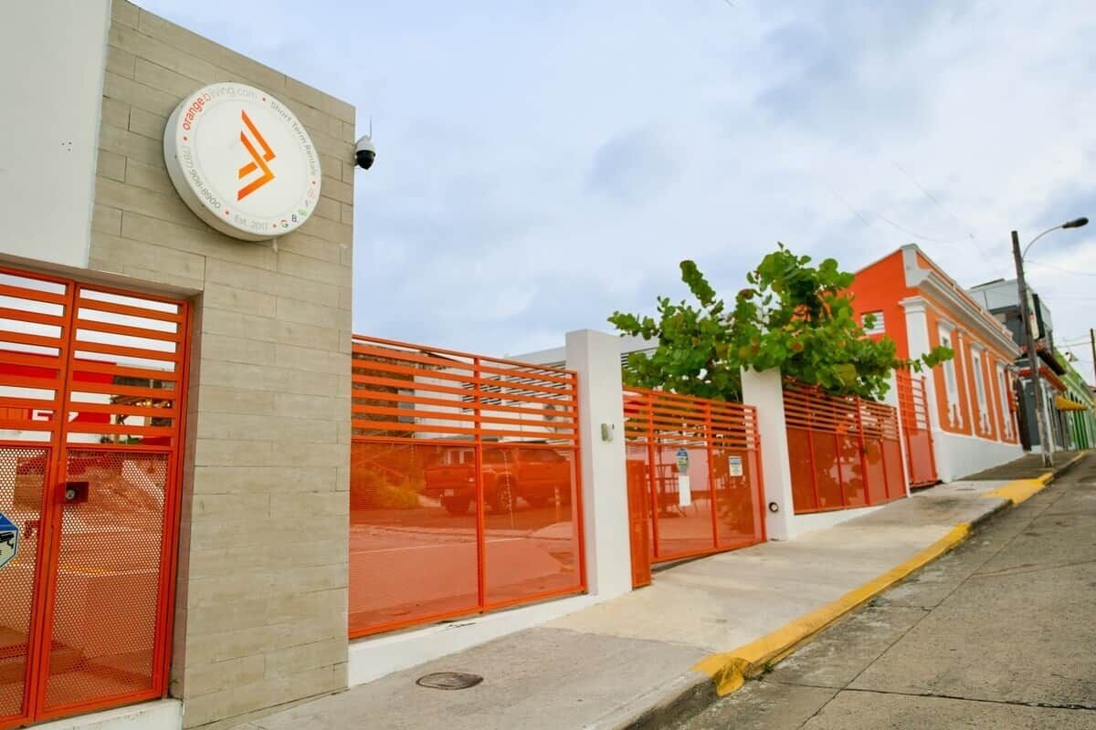 A building with a beige facade, red gates, and a clock on the wall.