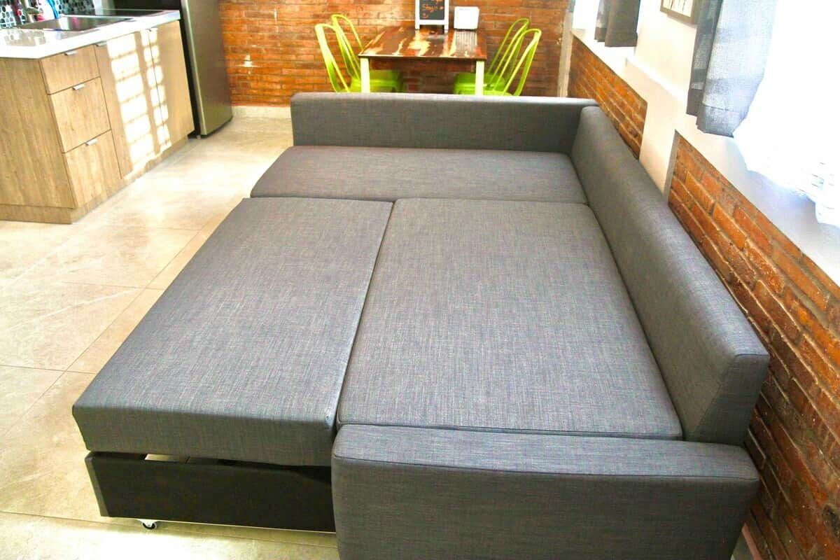 Une cuisine moderne avec un canapé d’angle gris, une table à manger avec des chaises et un mur en briques.