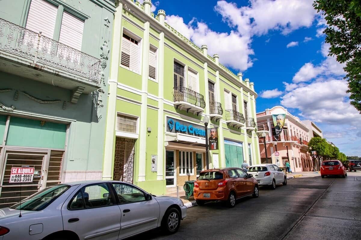 Vista de la calle con coches estacionados, el cine Rex y un edificio con un cartel que dice 'SE ALQUILA'.