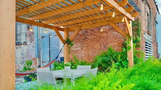 A covered outdoor seating area with a brick wall backdrop, wooden pergola, and hanging lights.