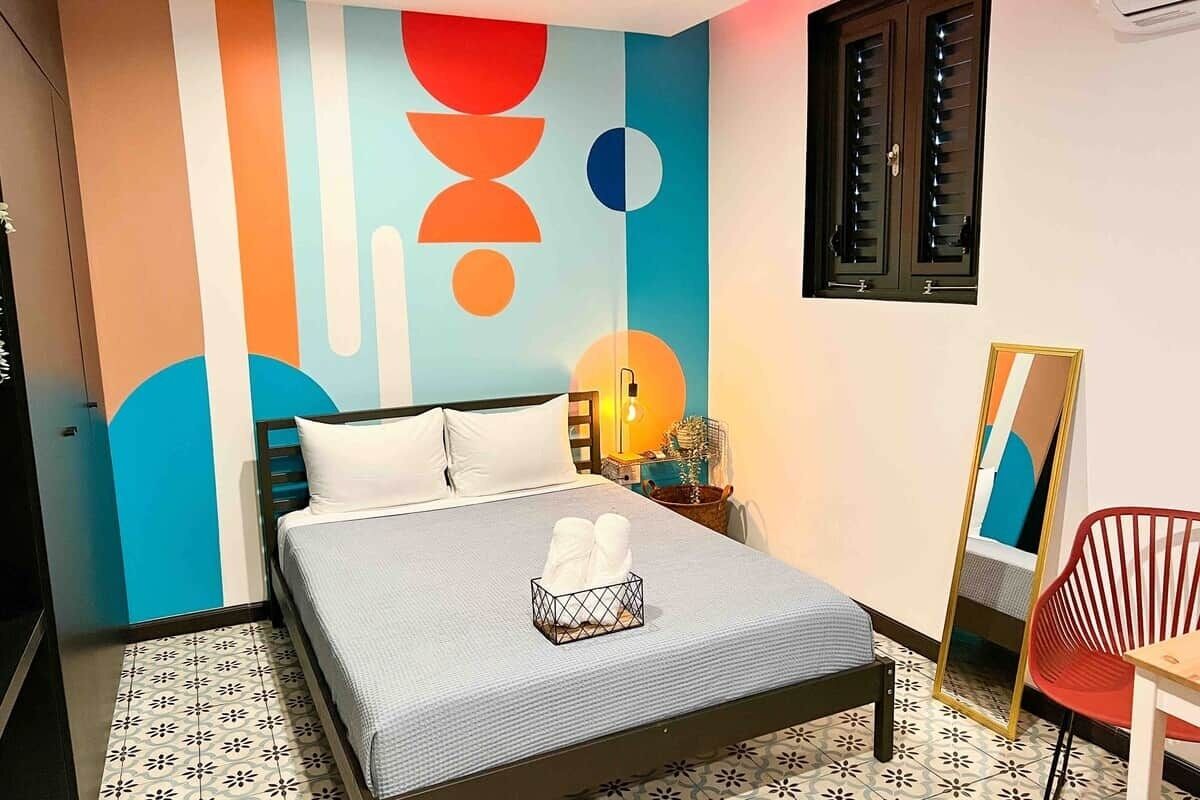 Ein Schlafzimmer mit einem Bett, einem Nachttisch mit Lampe, einem Spiegel und einem roten Sessel.