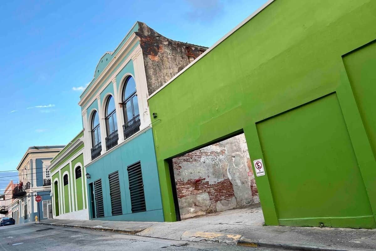 A street with buildings painted in green and blue, a clear sky, and a 'no parking' sign.