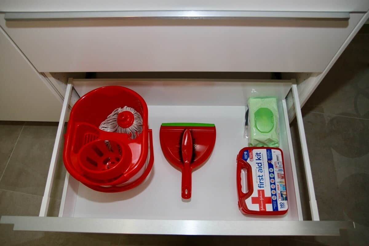 Uma gaveta com uma pá vermelha, uma vassoura verde e um kit de primeiros socorros.