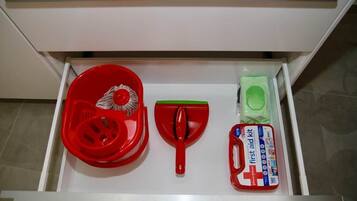 Uma gaveta com uma pá vermelha, uma vassoura verde e um kit de primeiros socorros.