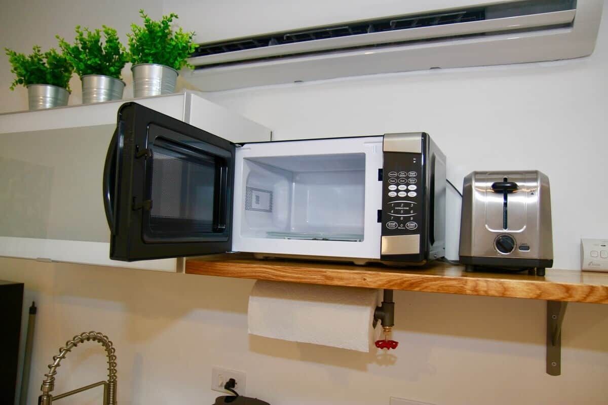 A kitchen with a microwave, toaster, and potted plants on a shelf.