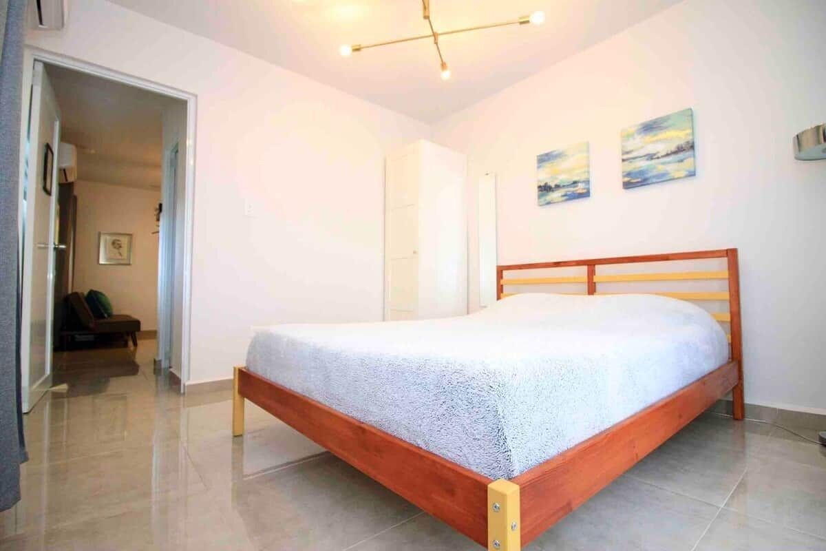 A bedroom with a wooden bed, a door leading to another room, and two wall-mounted paintings.