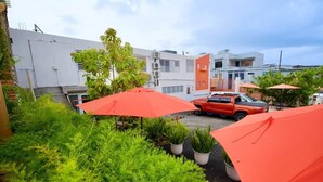 A parking area with red umbrellas, potted plants, and a red SUV. - 1.7 • Balcony • Generator • Parking • 2nd Floor (Mayagüez)