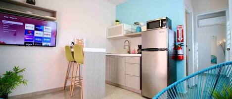 Una cocina compacta equipada con microondas, refrigerador y un televisor de pantalla plana que muestra servicios de transmisión.