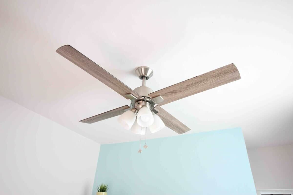 Ventilador de teto com lâminas de madeira e luminária em um quarto com paredes azul-claras.