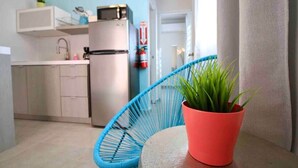 A kitchenette with a refrigerator, a sink, and a blue chair with a potted plant.