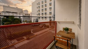 A balcony with a red mesh partition, a small wooden table, and a potted plant.