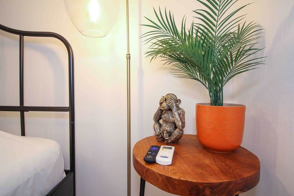 Ein Bett, ein kleiner runder Holztisch mit Fernbedienung, eine dekorative Affiguren und ein Blumentopf.