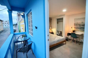 Et værelse med seng, skrivebord, stol og en balkon med bord og stole.