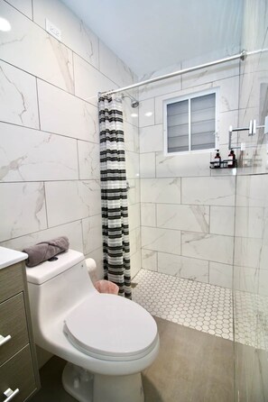 Et badeværelse med toilet, en bruser med stribet gardin og flisegulv.