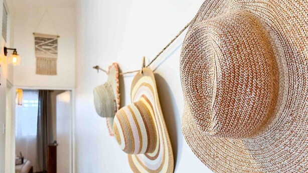 Une pièce dans laquelle on peut voir un grand chapeau tressé accroché au mur, une tapisserie murale tressée et un objet en bois.