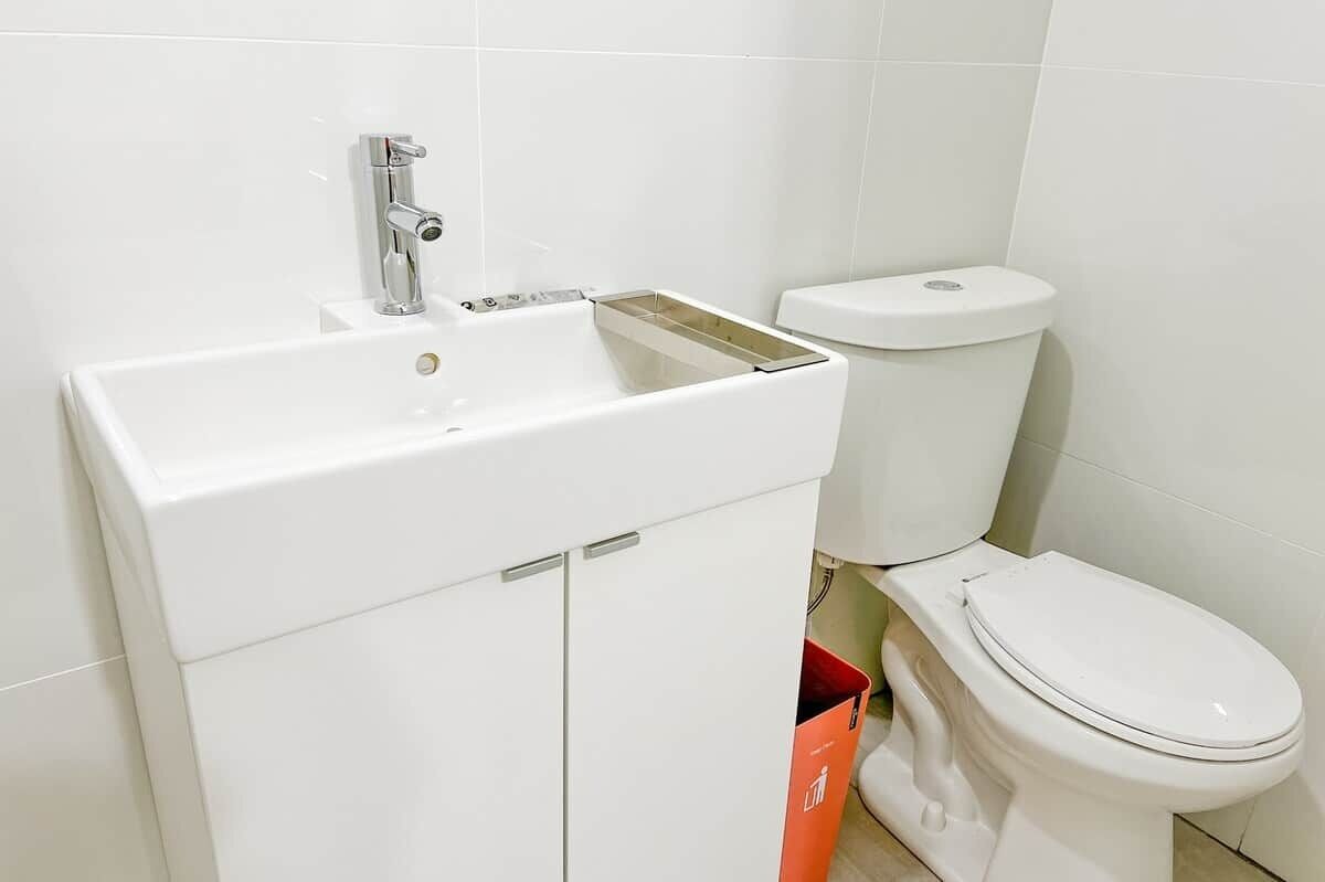 A bathroom with a white sink, a toilet, and a red trash bin.